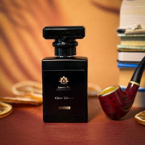 May include: A black bottle of Amon-Ra Citrus Tobacco perfume with a gold label and a black cap. The bottle is sitting on a red surface with a pipe and orange slices.