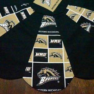 May include: Black and gold Western Michigan Broncos themed fabric with a repeating pattern of the team logo and "WMU" on a black background. The fabric is cut into a unique shape, possibly for a table runner or decorative piece.