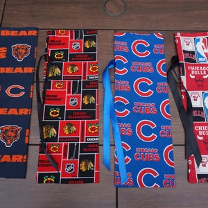 May include: Four fabric bookmarks featuring sports team logos. One navy blue bookmark has orange text and a bear logo. Another has a red and black design with the text "Chicago Blackhawks". The third is blue with "Chicago Cubs" text. The last is red with "Chicago Bulls" text.