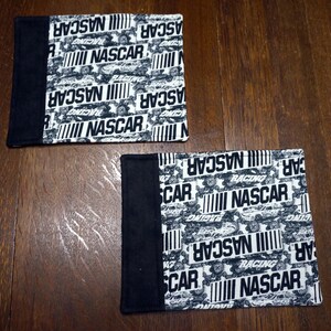 May include: Two square fabric items with a black and white NASCAR racing theme. The main pattern features the word "NASCAR" in bold white letters, along with racing car graphics. A solid black border is on one side of each item.
