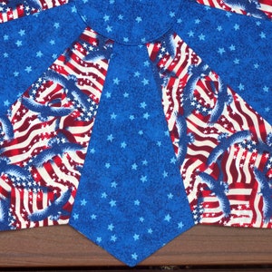 May include: A patriotic textile featuring a design with the American flag and eagles. The fabric has a blue background with white stars, and sections with red and white stripes and blue eagles.