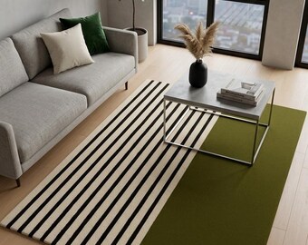May include: A modern area rug with a striking design. The rug features a section of black and white stripes and a solid olive green section. The rug is placed in a living room setting with a gray sofa and a coffee table.