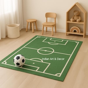 Puede incluir: Alfombra rectangular verde con dise&ntilde;o de campo de f&uacute;tbol blanco y un bal&oacute;n de f&uacute;tbol. La alfombra tiene el texto "Indian Art & Decor" en blanco. La alfombra est&aacute; sobre un suelo de madera clara.