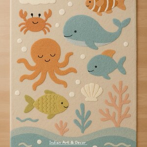 May include: A rectangular area rug with a beige background featuring a tufted ocean theme. The design includes a blue whale, an orange octopus, a crab, various fish, a seashell, and coral. The text Indian Art & Decor is printed at the bottom.