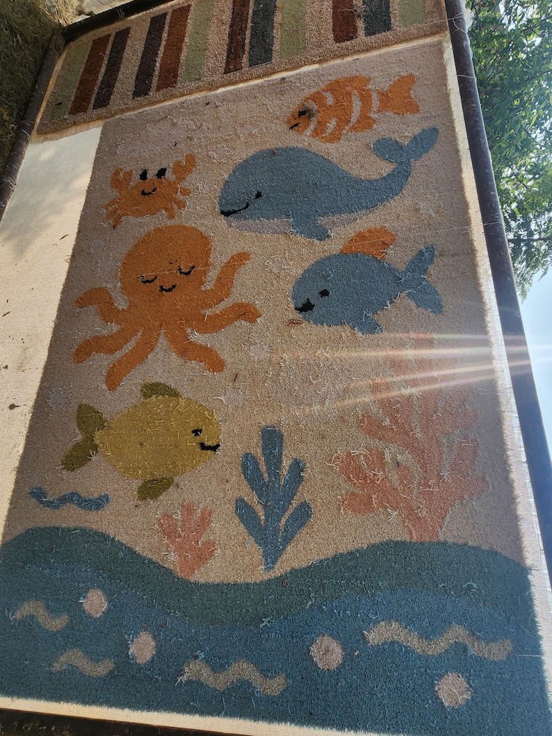 May include: A rectangular coir doormat featuring a tan background with a colorful marine life pattern. The design includes a blue whale, an orange octopus, a crab, and various fish in shades of blue, yellow, and orange, alongside coral and wave motifs.