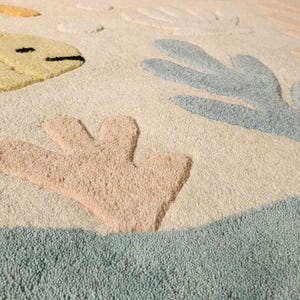 May include: A tufted area rug featuring a cream-colored background with raised, textured motifs of a yellow fish, light blue coral, and peach-colored coral. The design includes soft, muted tones and a plush, high-pile surface texture throughout.