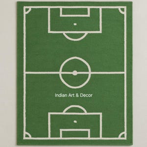 Puede incluir: Alfombra rectangular verde con un dise&ntilde;o de campo de f&uacute;tbol blanco. La alfombra presenta un contorno detallado del campo, incluyendo el c&iacute;rculo central, las &aacute;reas de penalti y las marcas de esquina. El texto "Indian Art & Decor" est&aacute; en la parte inferior.