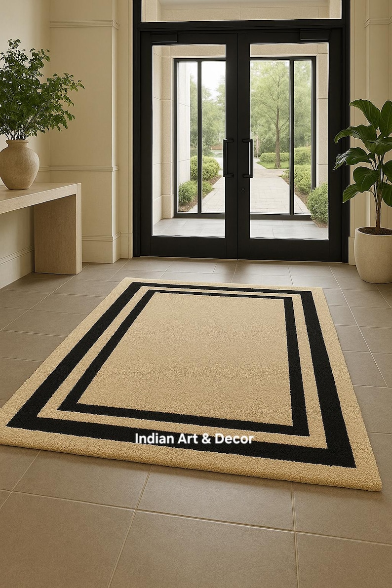 May include: A rectangular area rug featuring a solid beige center framed by a thick black border. The rug has a textured surface and includes the white text Indian Art & Decor printed on the lower section of the black border area.