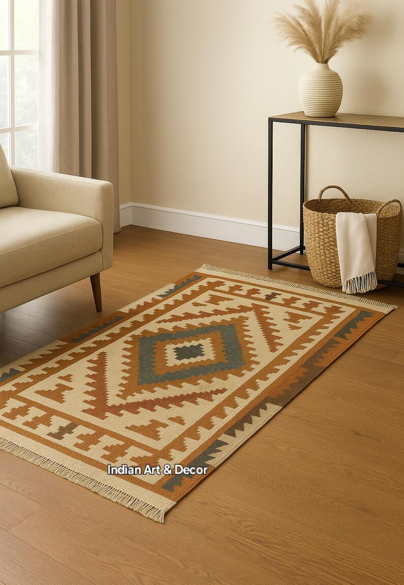 May include: Rectangular area rug with a geometric pattern in beige, brown, and teal. The rug has a fringed edge and is placed on a hardwood floor. The text "Indian Art & Decor" is visible.