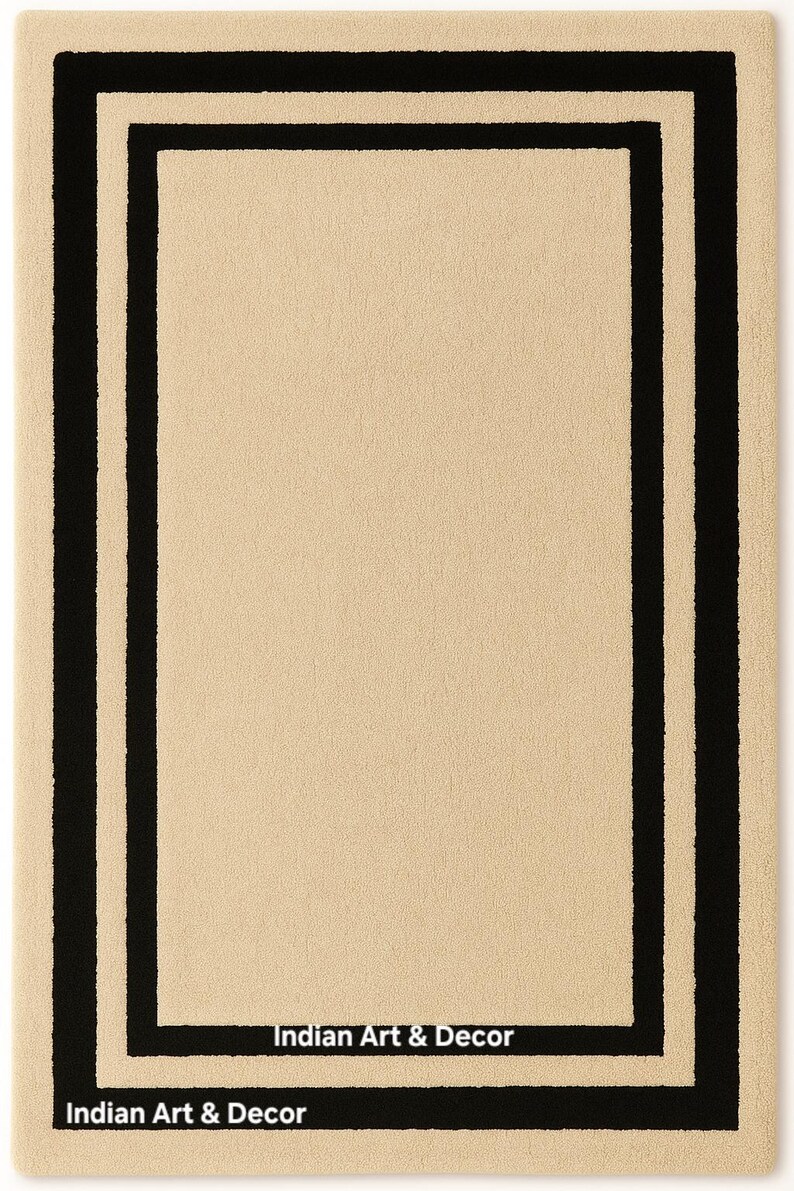 May include: A rectangular area rug featuring a solid beige center bordered by a thick black rectangular frame and an outer beige border. The text Indian Art & Decor is printed in white on the bottom black border and the bottom center black line.