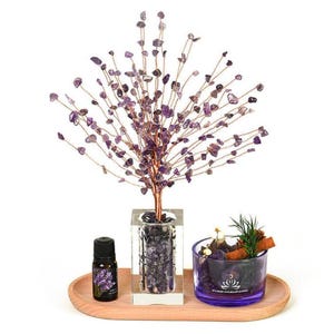 May include: A decorative amethyst gemstone tree with copper wire branches, displayed with a small essential oil bottle and a glass jar with potpourri. The items are arranged on a wooden tray, creating a serene and natural aesthetic.