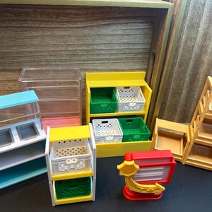 Pode incluir: Miniaturas de brinquedos para exposição de mercearia. Inclui uma vitrine azul e transparente, prateleiras amarelas e brancas com caixas verdes e brancas, uma caixa registradora vermelha e uma prateleira de madeira.