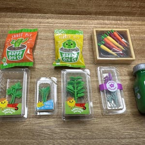 Pode incluir: Uma coleção de suprimentos de jardinagem em miniatura, incluindo pacotes de sementes, mudas em recipientes transparentes, uma caixa de cenouras e uma garrafa de água verde. Os pacotes de sementes são rotulados como "Happy Gro Co" e "Sandy Mix".
