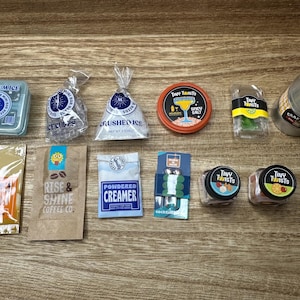 Pode incluir: Uma coleção de alimentos e bebidas em miniatura, incluindo cubos de gelo, gelo picado, café, creme, ingredientes para coquetéis e um pequeno barril. Os itens estão dispostos em uma superfície de madeira, com vários rótulos e embalagens.