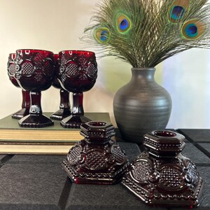 Peut inclure: Quatre gobelets en verre rouge avec un motif en diamant et deux bougeoirs en verre rouge avec un motif en diamant. Les gobelets et les bougeoirs sont sur une surface noire avec un livre en arrière-plan. Un vase avec des plumes de paon est en arrière-plan.