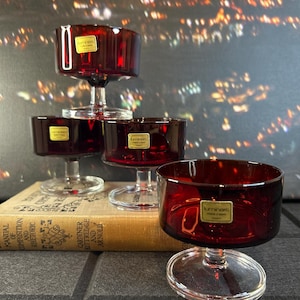 May include: Four red glass dessert dishes with clear glass stems and bases. The dishes are stacked on top of each other. The dishes have a gold label that says "Luminous" on them.