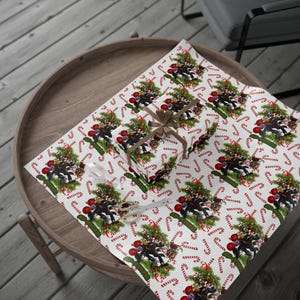 Op de afbeelding: Wit inpakpapier met een herhalend patroon van snoepstokken, hulst en een groep cartoonfiguren die kerstmanmutsen dragen. De figuren staan voor een kerstboom.