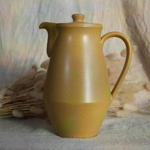 May include: A ceramic coffee pot with a lid and a handle. The pot is a light brown colour with a slightly greenish hue.