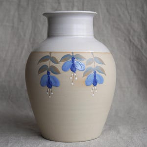 May include: A ceramic vase with a cream-coloured body and a white rim. The vase is decorated with three blue and white flowers.