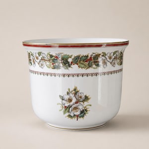 May include: A white ceramic planter featuring a decorative band of green holly leaves and red berries around the top rim. The exterior is adorned with a central floral motif of white flowers, green leaves, and red berries, finished with a gold rim.