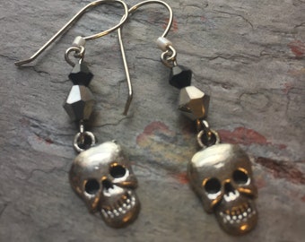 May include: A pair of drop earrings featuring silver-toned metal skull charms suspended from silver-toned ear wires. Each earring is accented with a small black faceted bead and a larger metallic silver faceted bead above the skull charm.