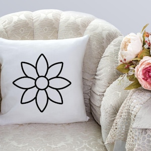 Pode incluir: Uma almofada branca com um contorno preto de uma flor sobre ela. A almofada est&aacute; sentada em uma poltrona branca.
