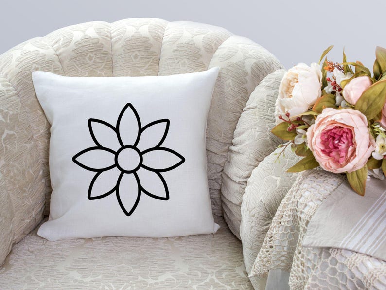Pode incluir: Uma almofada branca com um contorno preto de uma flor sobre ela. A almofada est&aacute; sentada em uma poltrona branca.