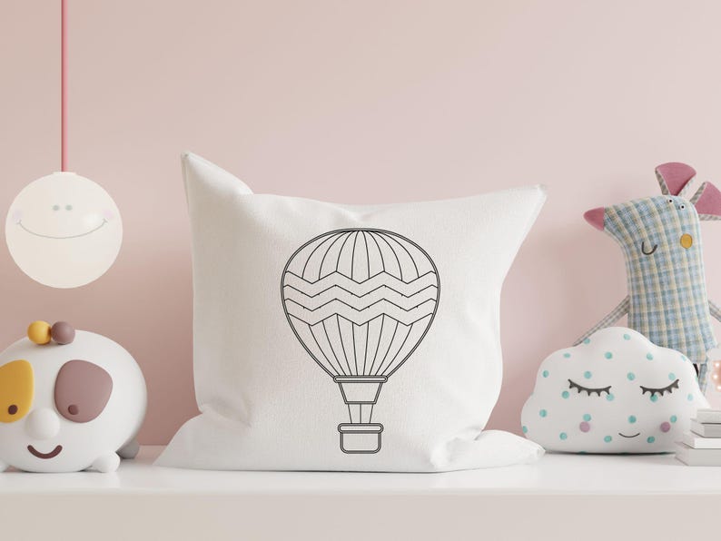 May include: A white pillow with a black outline of a hot air balloon with a wavy pattern. The pillow is on a light pink surface.