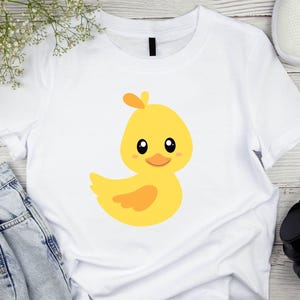 May include: A white t-shirt with a yellow cartoon duckling with orange accents. The duckling has big eyes and a small beak.