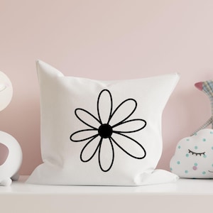 Pode incluir: Uma almofada branca com um desenho de margarida preta. A almofada est&aacute; numa prateleira com outros artigos decorativos.