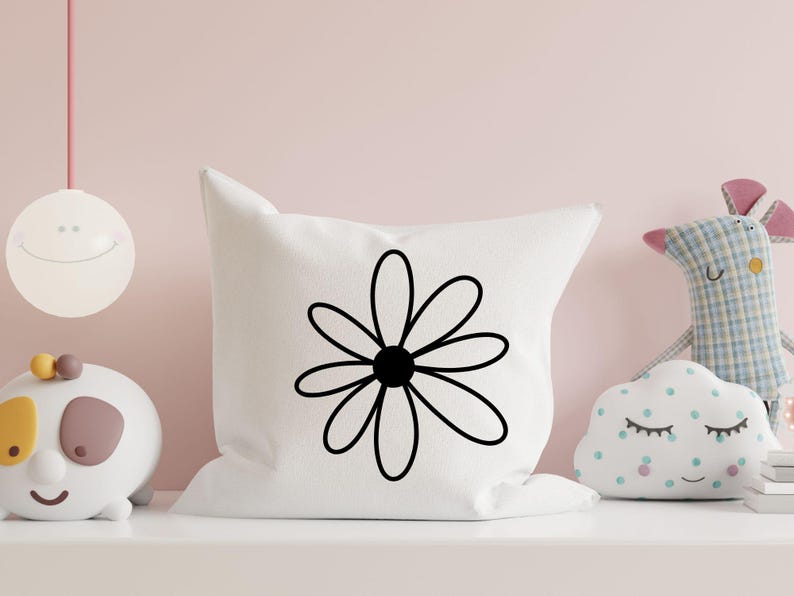Pode incluir: Uma almofada branca com um desenho de margarida preta. A almofada est&aacute; numa prateleira com outros artigos decorativos.