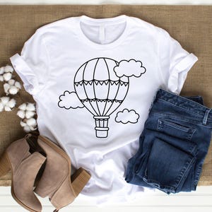 May include: A white t-shirt with a black outline of a hot air balloon and clouds. The balloon has a basket and is surrounded by clouds.