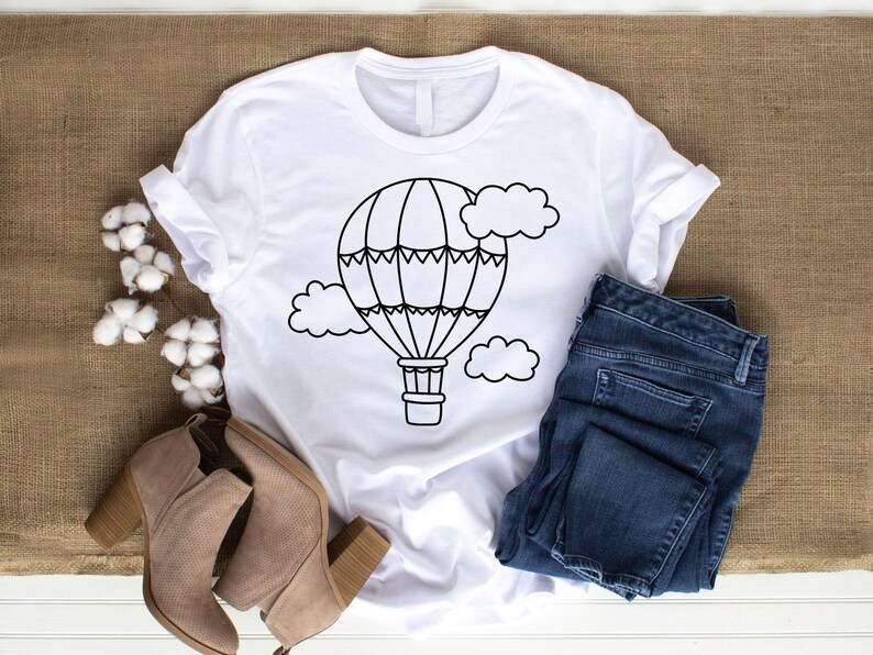 May include: A white t-shirt with a black outline of a hot air balloon and clouds. The balloon has a basket and is surrounded by clouds.