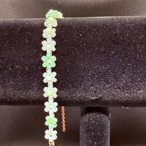 May include: A green and white beaded bracelet with a flower design and a silver clasp.