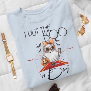May include: Light blue sweatshirt with a ghost wearing sunglasses and holding a pumpkin and a coffee cup. The text on the shirt reads "I put the boo in bouji".