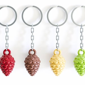 May include: Four keychains with pinecone-shaped charms in red, brown, yellow, and green. Each charm is attached to a silver chain and ring. The background is plain white.