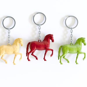 May include: Three horse keychains with silver key rings and chains. The horses are in different poses and are painted in yellow, red, and green.