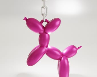 Puede incluir: Una escultura de perro globo de color magenta colgando de una cadena plateada. El perro está hecho de formas de globos conectadas, con un acabado liso y brillante. La escultura está suspendida sobre un fondo blanco.