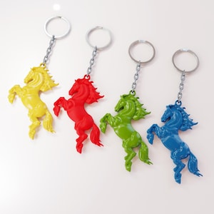 May include: Four colorful horse keychains. The keychains feature a yellow, red, green, and blue horse design. Each horse is attached to a silver chain and ring. The horses are in a rearing pose.