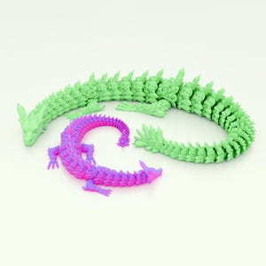Puede incluir: Dos dragones estilizados, uno verde y otro morado, están enroscados en un círculo sobre un fondo blanco. Los dragones están hechos de un material texturizado y tienen una apariencia espinosa y escamosa.
