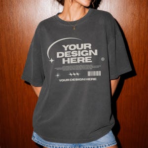 Könnte beinhalten: Ein anthrazitfarbenes Kurzarm-T-Shirt mit einem hellgrauen Grafikdruck. Das Design enthält den Text "YOUR DESIGN HERE" in einer serifenlosen Schrift, eine geschwungene Linie, Sternsymbole, eine Strichcode-Grafik und wiederholten Text.