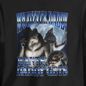 May include: Black t-shirt featuring a graphic of a wolf in a hat, a werewolf, and the text "WHATEVER DADDY WANTS DADDY GETS" in blue. The design is set against a full moon backdrop.
