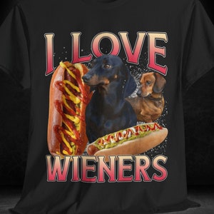 Op de afbeelding: Zwart T-shirt met een afbeelding van twee teckels en hotdogs. De tekst "I LOVE WIENERS" staat op het shirt gedrukt.