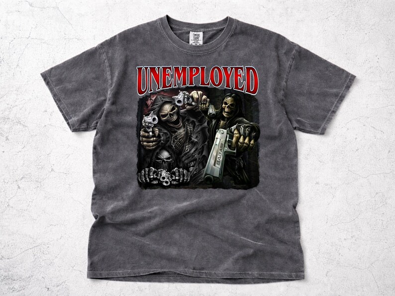 May include: A gray t-shirt featuring the word "UNEMPLOYED" in red above a graphic of skeletal figures holding guns. The graphic has a dark, distressed aesthetic, with the word "BAD ASS" visible on one of the guns.