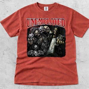 May include: A red-orange t-shirt featuring the word "UNEMPLOYED" in red, arched text. The graphic depicts skeletal figures holding guns. The design is printed on a soft, short-sleeved tee.