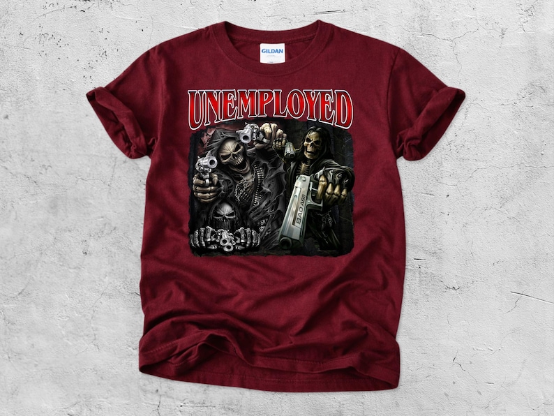 May include: Maroon t-shirt with the word "UNEMPLOYED" in red and white lettering. The graphic depicts a skeletal figure holding a gun, with other skulls and guns. The shirt is made of a soft material.