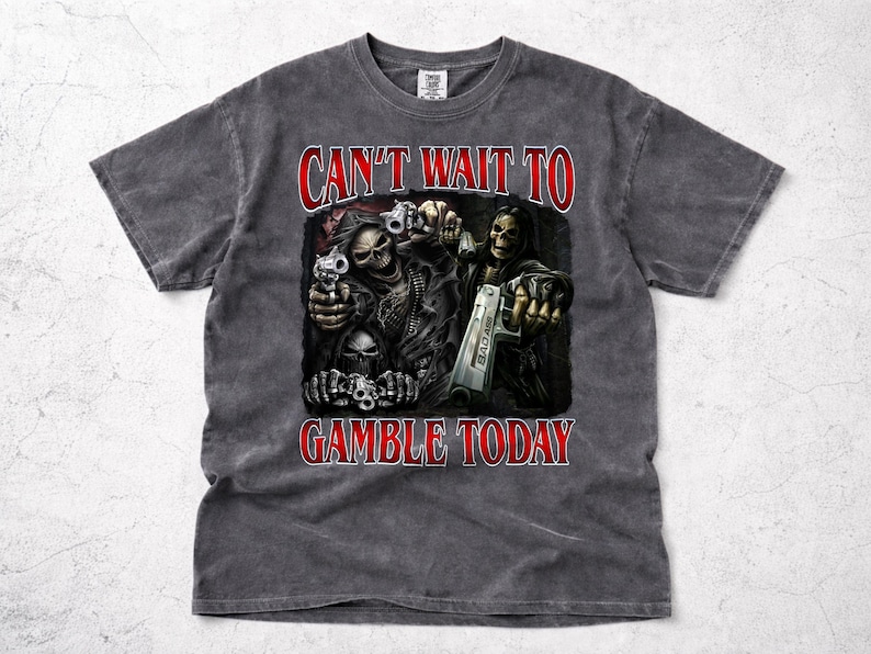 May include: Dark grey t-shirt featuring a graphic of skeletal figures holding guns, with the text "CAN'T WAIT TO GAMBLE TODAY" in red. The design is centered on the front of the shirt, with a vintage wash effect.