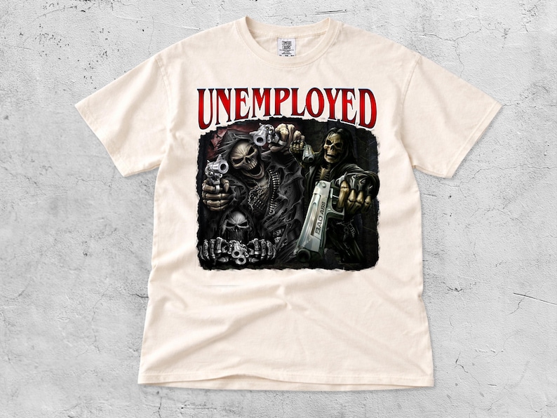 May include: Cream-colored t-shirt featuring a graphic of two skeletal figures holding guns, with the word "UNEMPLOYED" in red above them. The design includes skulls and the text "BAD ASS" on one of the guns.