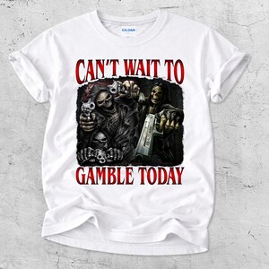 May include: White t-shirt with a graphic featuring skeletal figures holding guns, with the text "CAN'T WAIT TO GAMBLE TODAY" in red. The design is centered on the shirt.