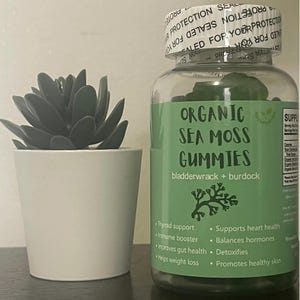 May include: A clear glass bottle with a green label that reads "Organic Sea Moss Gummies Bladderwrack + Burdock". The label lists several health benefits, including thyroid support, immune booster, and heart health. The bottle is filled with green gummies.
